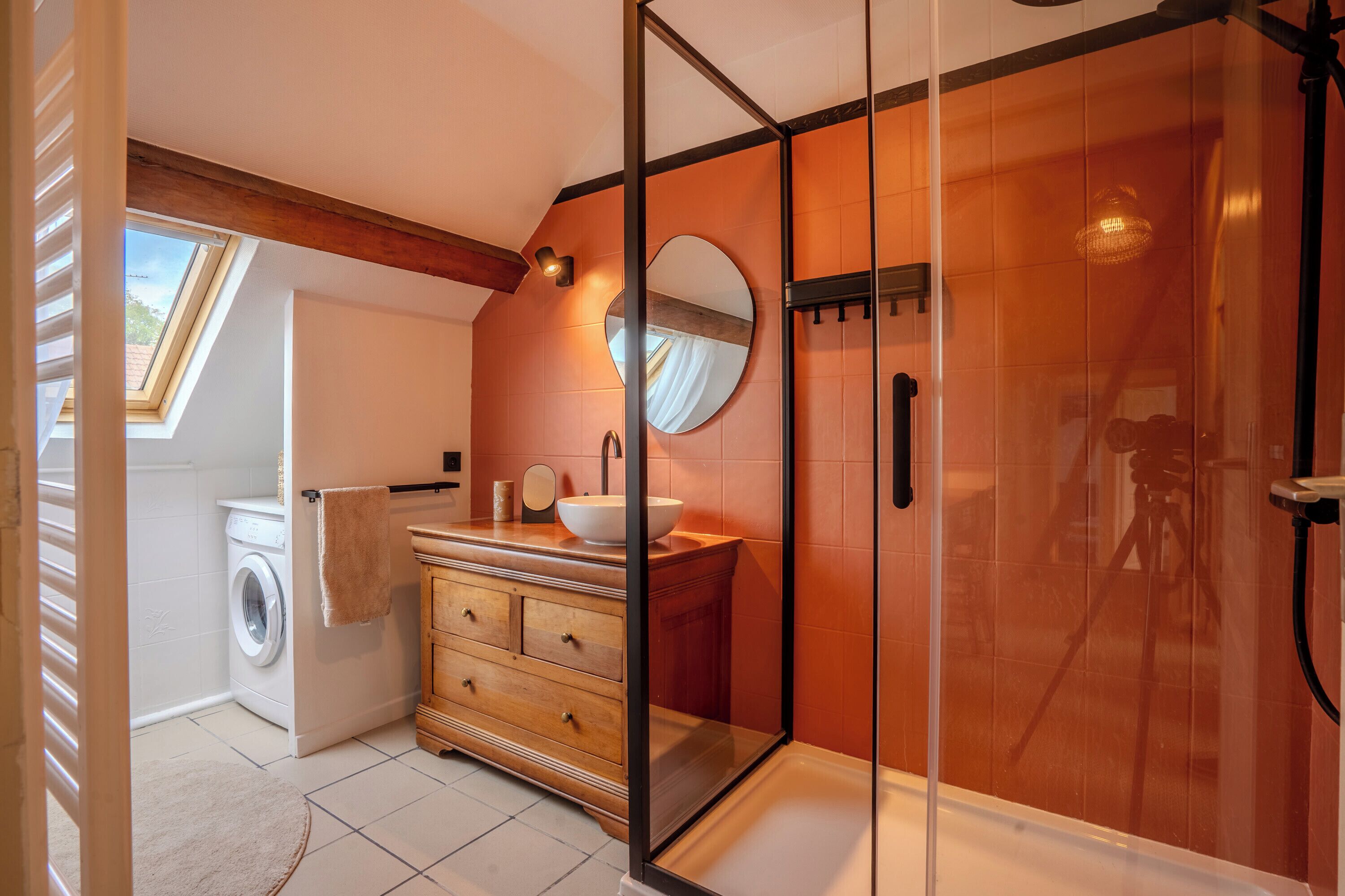Un baño moderno con ducha acristalada, tocador de madera, lavadora y tragaluz.