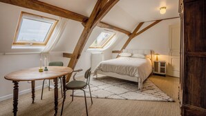 Een slaapkamer met een schuine balkenplafond, een bed, nachtkastje, lamp, stoel en een tafel met kaarsen.