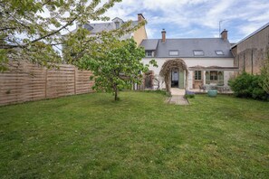 A residential property with a well-maintained lawn, a wooden fence, and a house with a sloped roof and chimneys. - Break en Sarthe - Wifi - Jardin (Bessé-sur-Braye)