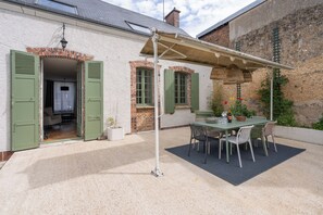A covered patio with a table and chairs, a brick wall, and a door leading to an interior space. - Break en Sarthe - Wifi - Jardin (Bessé-sur-Braye)