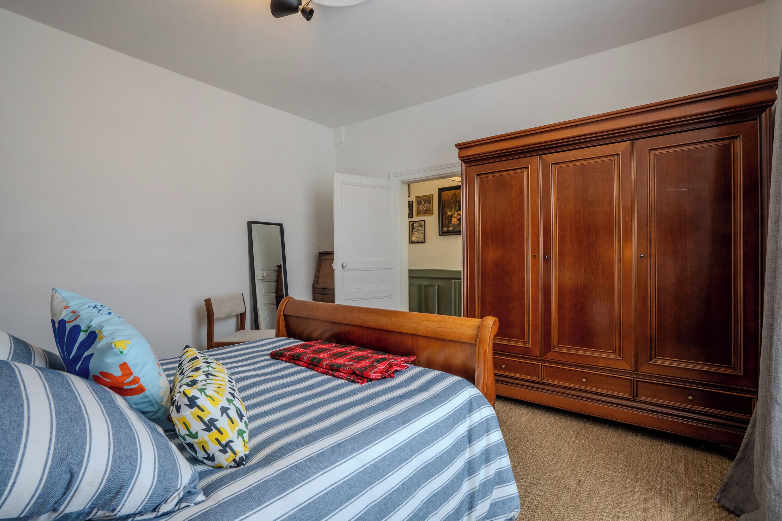 Une chambre à coucher avec un lit, une armoire en bois et une porte donnant sur une autre pièce.