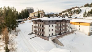 Ein mehrstöckiges Hotel mit Balkonen, eingebettet in eine verschneite Berglandschaft.