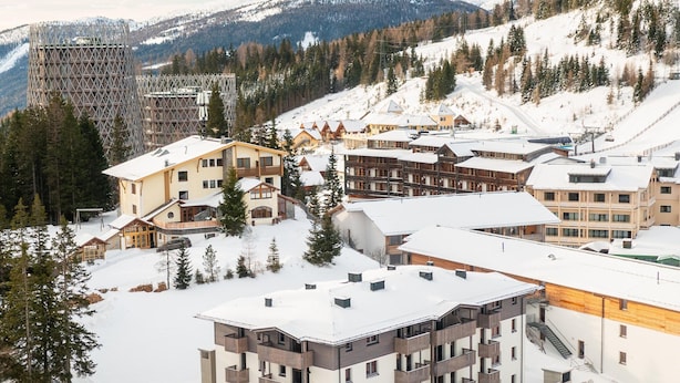 Ein schneeüberdeckter Hotelkomplex mit mehreren Gebäuden, darunter ein markantes mehrgeschossiges Haus mit Balkonen.