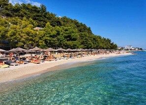 A beach with clear water, umbrellas, and people sunbathing. - One-bedroom Apartment With sea View (Rogoznica)