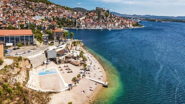 A coastal town with a beach, a castle on a hill, and a mix of residential and commercial buildings. - Apartment in Sibenik Near Adriatic Beaches (Sibenik)