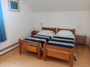 Une chambre avec deux lits en bois, une petite table de chevet, une lampe fixée au mur et un tableau encadré.