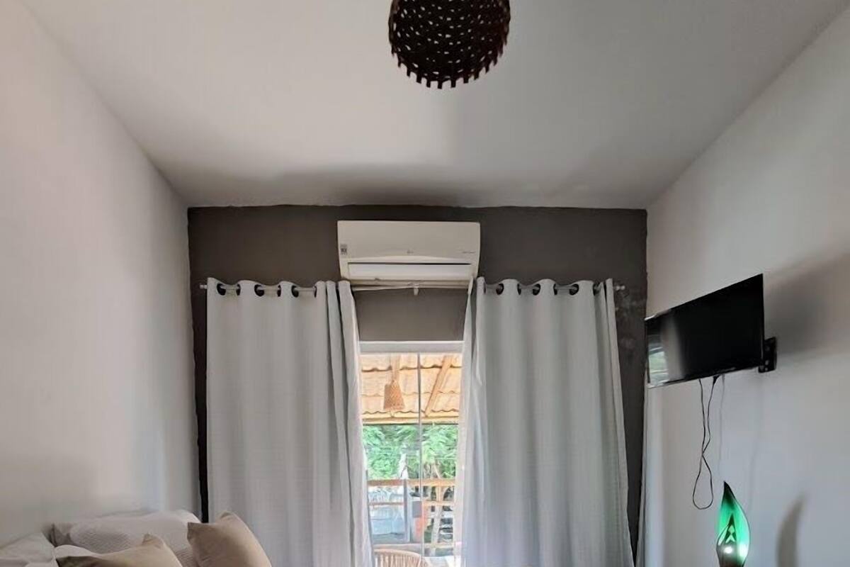 Une chambre à coucher avec un lit, des oreillers, un bureau, une télévision et une fenêtre avec des rideaux.