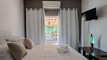 Un dormitorio con cama, almohadas, escritorio, televisor y ventana con cortinas.