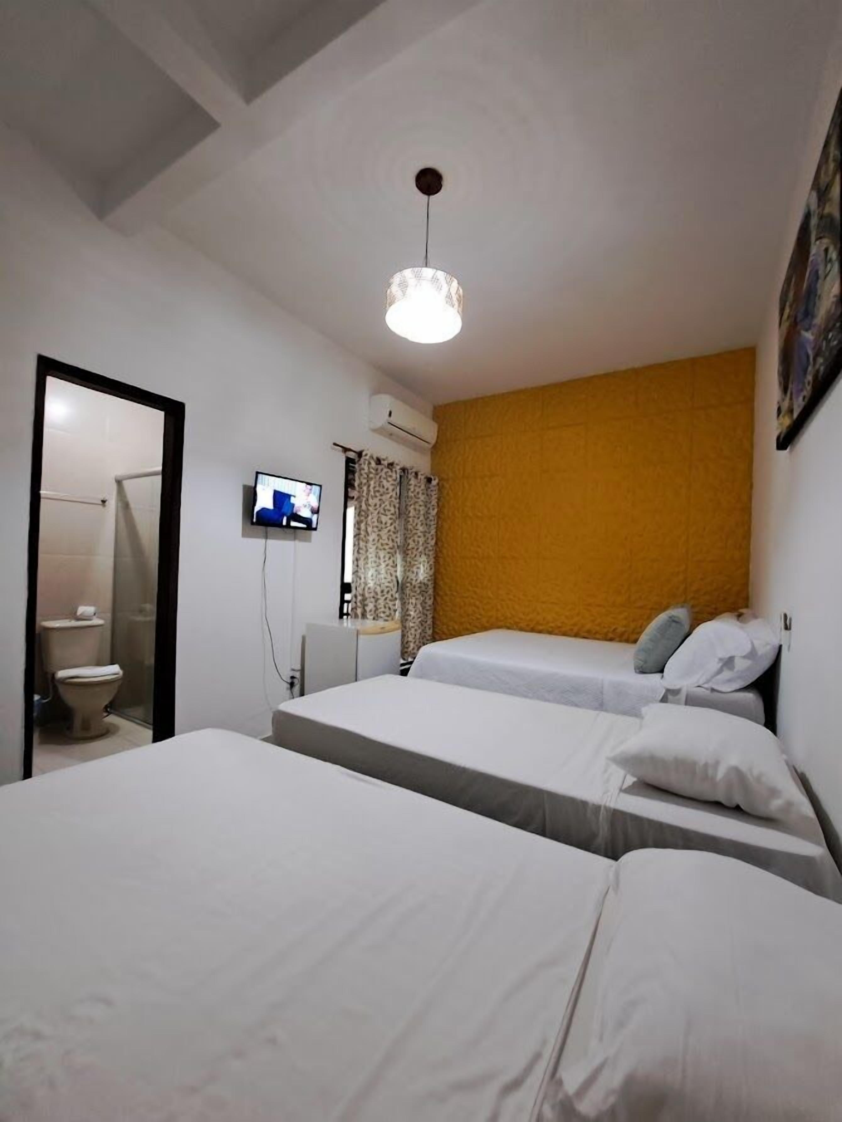 A hotel room with two beds, a television, an air conditioning unit, and a bathroom visible through an open door.