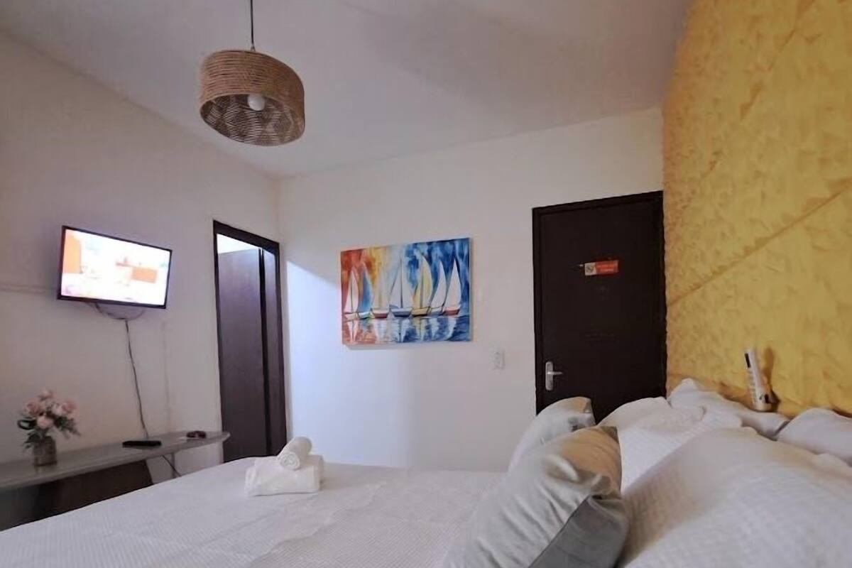 Une chambre à coucher avec un lit, des oreillers, une télévision, un tableau et une porte.