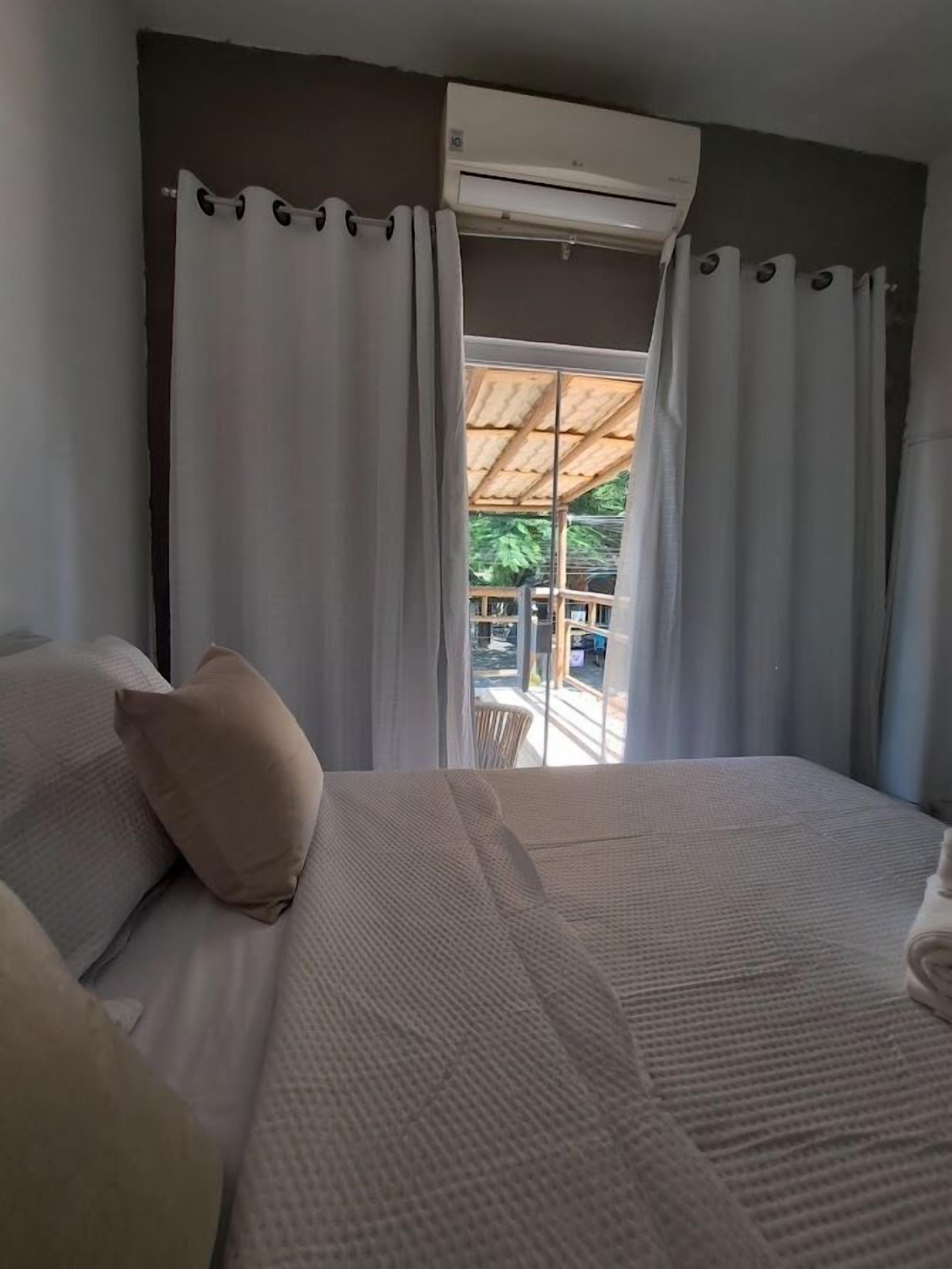 A bedroom with a large bed, white curtains, and an air conditioning unit.
