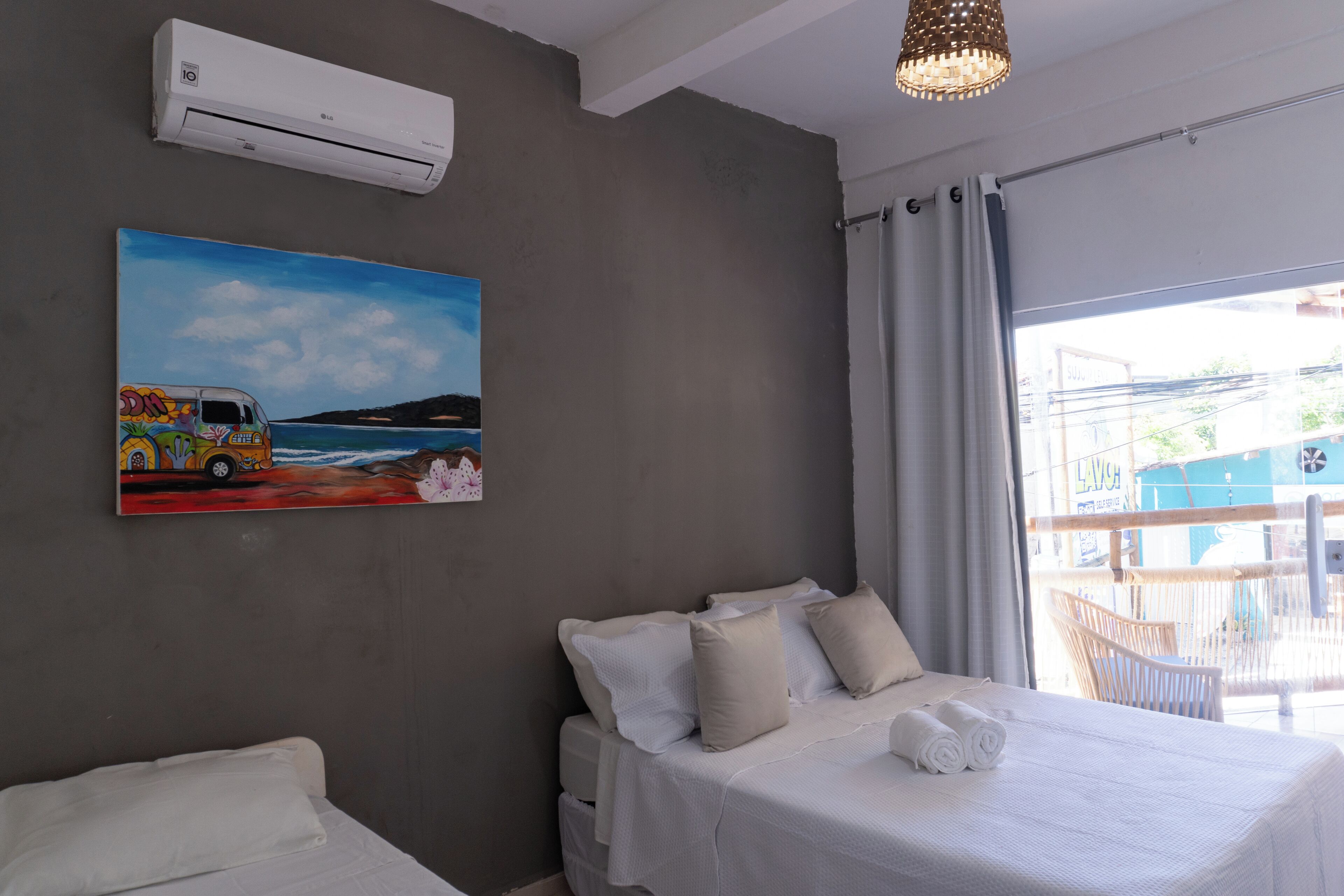 Quarto de hotel com uma cama, um quadro de uma van colorida, ar condicionado e vista para o exterior.