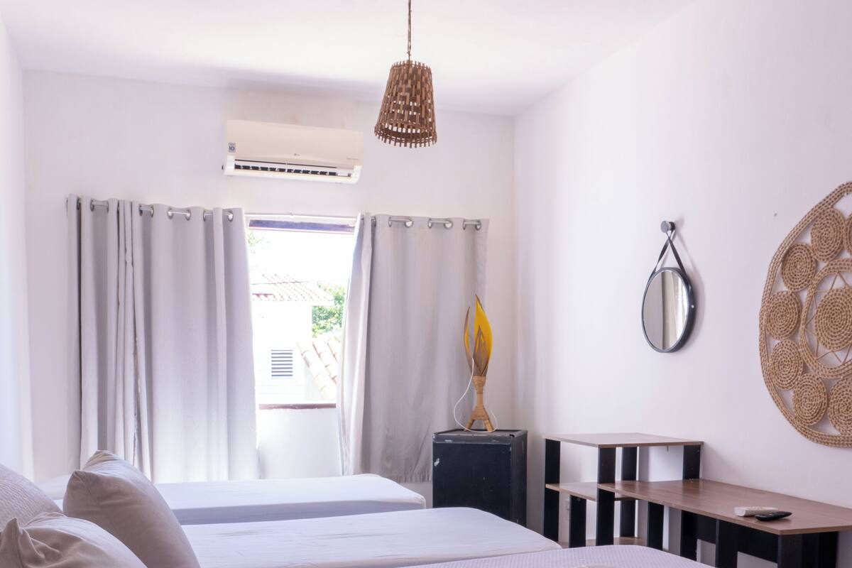 Une chambre d’hôtel avec deux lits, un bureau, une chaise, un miroir et un luminaire suspendu.