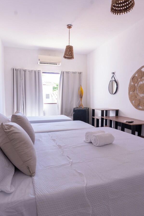 Une chambre d’hôtel avec deux lits, un bureau, une chaise, un miroir et un luminaire suspendu.