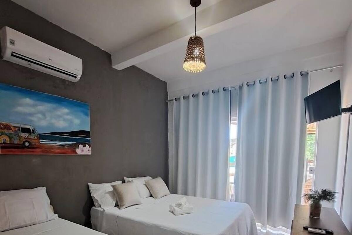 Une chambre d’hôtel avec deux lits, un tableau au mur, un appareil de climatisation, un bureau en bois et une fenêtre avec des rideaux.
