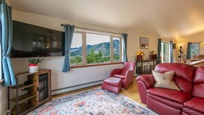 Ein Wohnzimmer mit großem Fenster, einem Flachbildfernseher, einem roten Ledersofa und einem gemusterten Teppich.