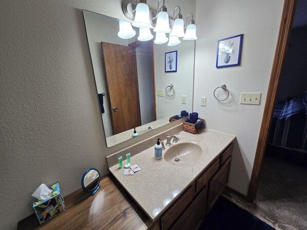A bathroom with a large mirror, a sink, and a vanity. There are towels and toiletries on the counter.