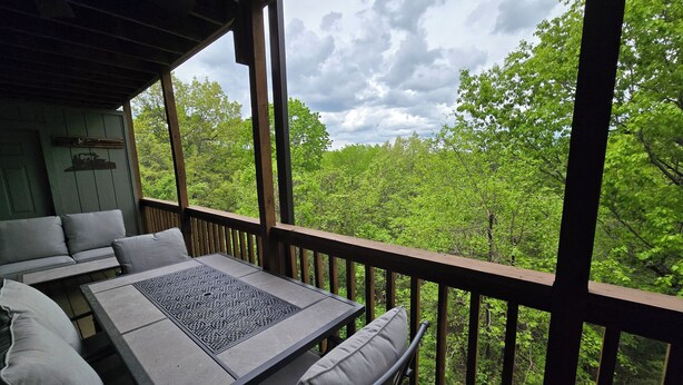 Un espacio de estar techado al aire libre con una mesa y sillas, con vistas a un paisaje boscoso.