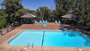 Una piscina rectangular con un trampolín, rodeada de sillas de descanso y zonas sombreadas.