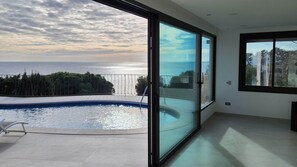 Een moderne kamer met een glazen deur naar een balkon met uitzicht op een zwembad en de zee.