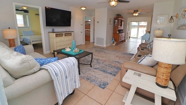 A living room with a sofa, coffee table, and TV. There is a ceiling fan, a lamp, and a door leading to another room. - Sunny house with pool, just steps to the beach! (Ormond Beach)