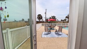 A view from a balcony to a pool area with chairs and a red umbrella. - Sunny house with pool, just steps to the beach! (Ormond Beach)