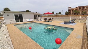 A rectangular pool with clear water, surrounded by a sandy area. There are red floating balls in the pool. - Sunny house with pool, just steps to the beach! (Ormond Beach)