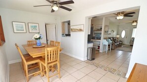 A dining area with a wooden table and chairs, a ceiling fan, and a kitchen in the background. - Sunny house with pool, just steps to the beach! (Ormond Beach)