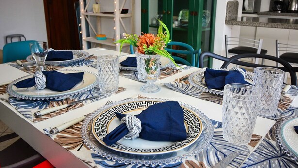 Una mesa de comedor dispuesta con servilletas azules, platos blancos y copas de vidrio transparente.