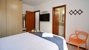 Una habitación de hotel con una cama, un armario de madera, un televisor montado en la pared y una pequeña silla naranja.