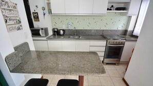 Una cocina con encimera de granito, armarios blancos, microondas, cafetera, lavabo y horno.
