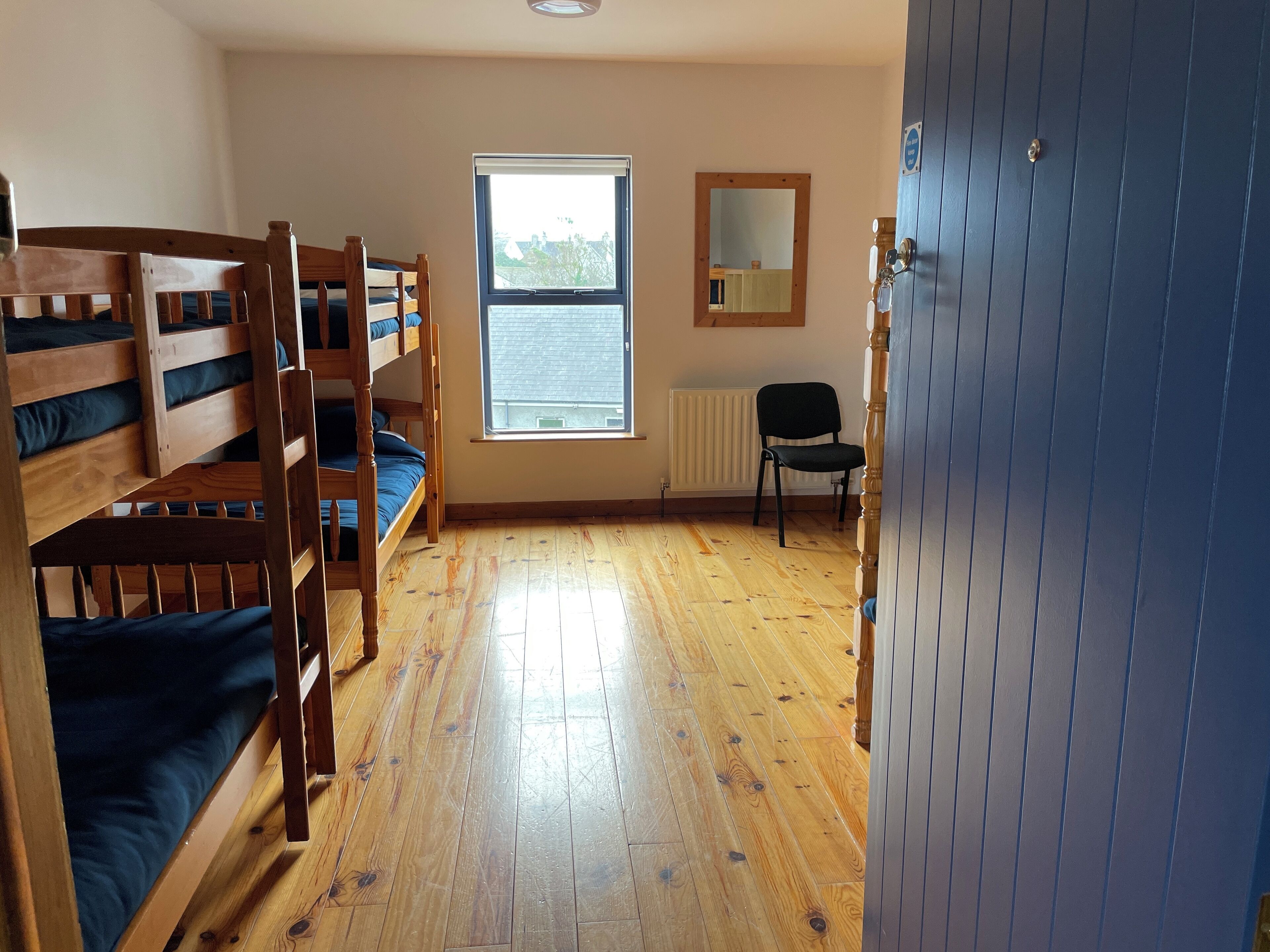 A dormitory room with bunk beds, a window, a radiator, and a chair.