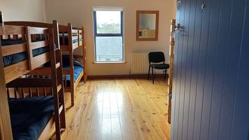 A dormitory room with bunk beds, a window, a radiator, and a chair.