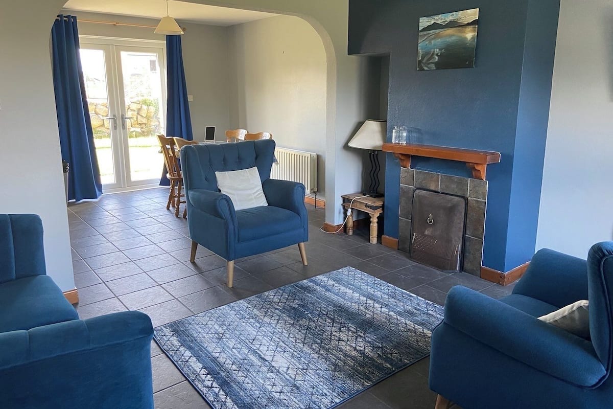 Ein Wohnzimmer mit blauem Sessel, einer Couch, einem Kamin und einem Essbereich mit Tisch und Stühlen.