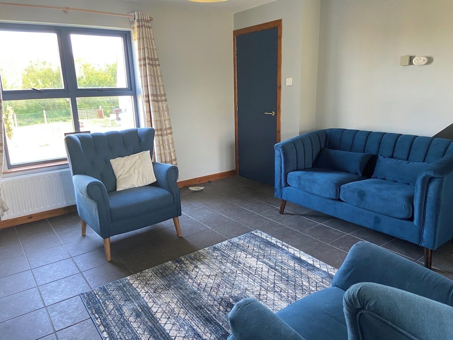 Una sala con un sillón azul, un sofá azul y una alfombra estampada.