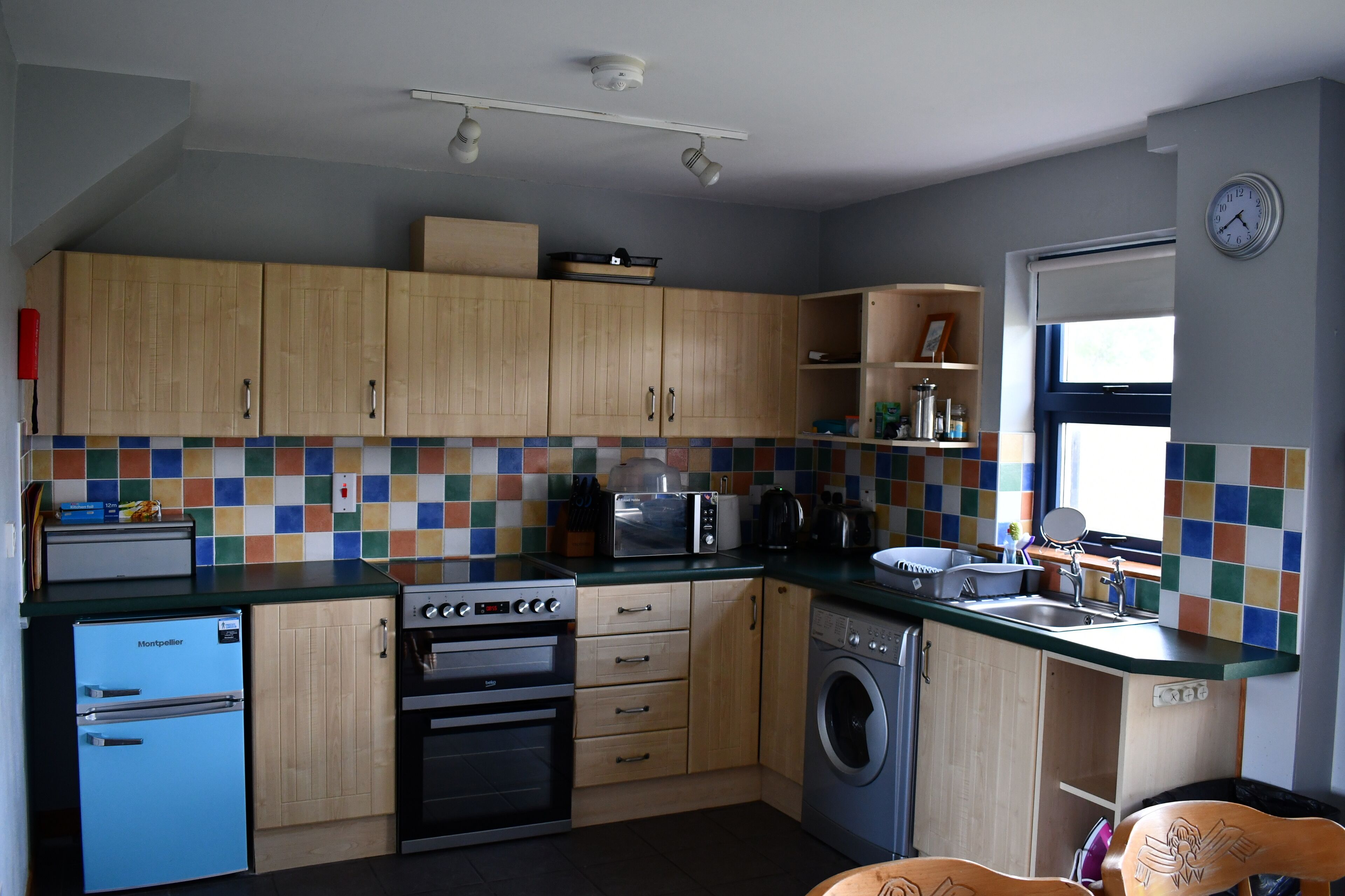 A compact kitchen with wooden cabinets, a microwave, a stove, a washing machine, and a refrigerator.