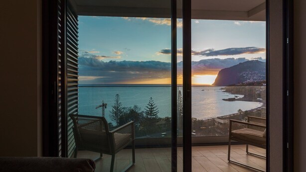 A balcony with a view of the sea and mountains during sunset. - GuestReady - Acqua Residences - Diamond (Funchal)