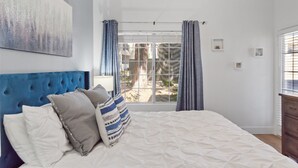 A bedroom with a large bed, a tufted headboard, a window with curtains, and a painting on the wall. - Barrett-Jackson| WestWorld| Heated Pool| Near Mayo (Scottsdale)
