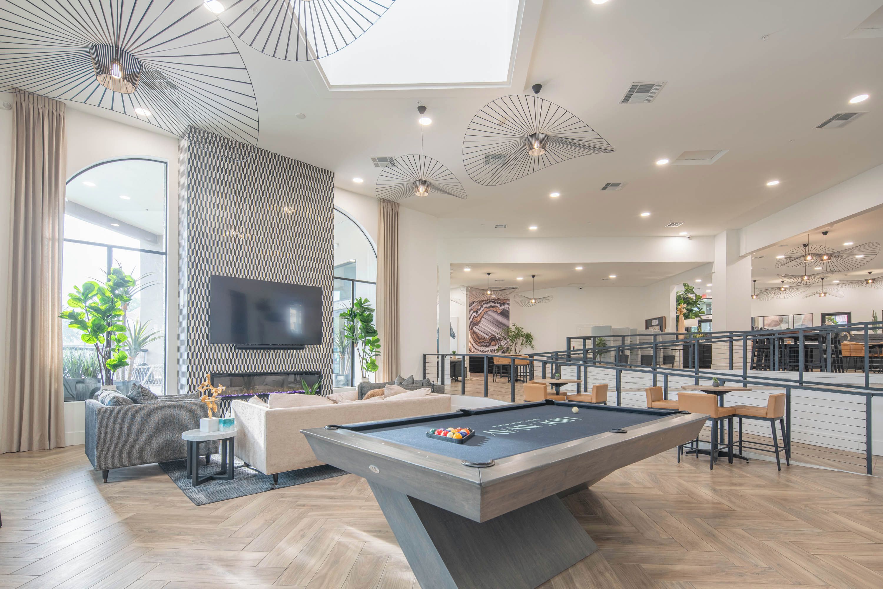 A modern living room with a pool table, comfortable seating, a flat-screen TV, and a dining area with bar seating.