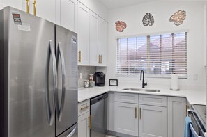 A modern kitchen with stainless steel appliances, white cabinetry, and a window with blinds.