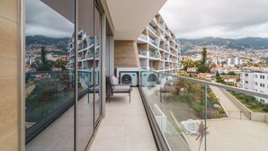 Un balcon moderne doté d’une balustrade en verre, d’un espace salon et offrant une vue sur le paysage urbain et les montagnes.