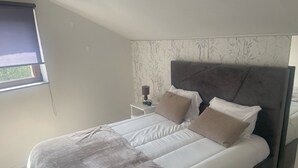A modern bedroom with a large bed, a nightstand, a lamp, and a window with a view. - Costa Guest House (Guimarães)
