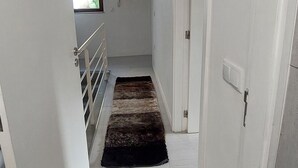 A narrow hallway with white walls, a wooden floor, and a dark brown rug. There are white doors on both sides, and a window at the end of the hallway. - Costa Guest House (Guimarães)