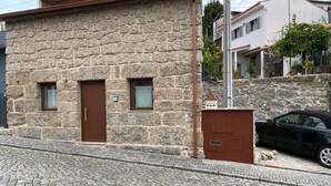 A stone building with two doors and windows, a cobblestone street, and a parked car. - Costa Guest House (Guimarães)