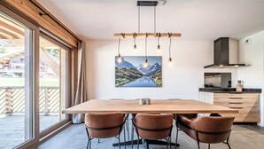 A modern kitchen with a wooden table and chairs, a large window, and a mountain landscape painting.