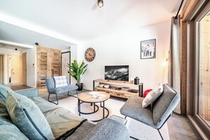 Ein modernes Wohnzimmer mit Sofa, Sessel, Couchtisch und Fernseher.