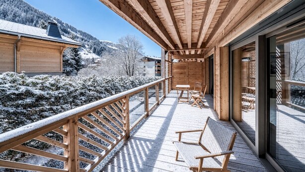 A wooden balcony with a view of snow-covered trees and buildings.