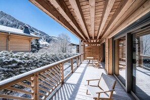 Un balcon en bois offrant une vue sur des arbres et des bâtiments recouverts de neige.