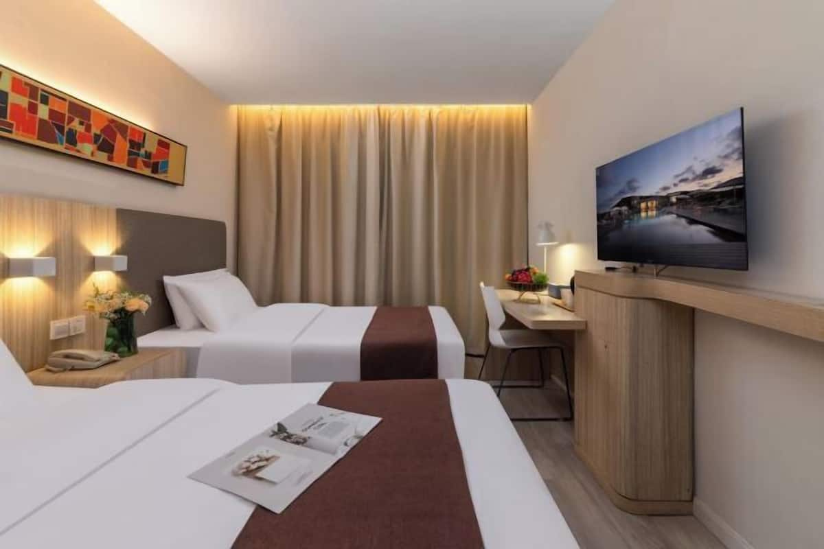 A hotel room with two beds, a desk, a TV, and a painting on the wall.