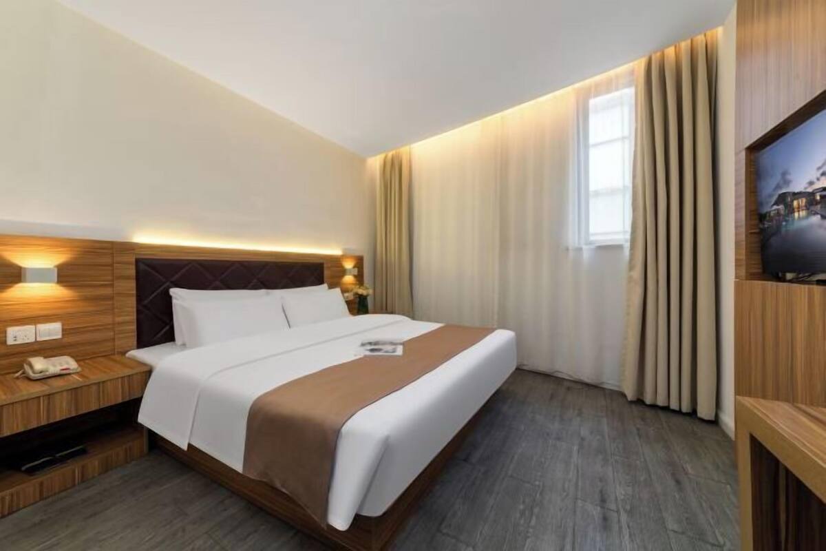 A hotel room with a bed, bedside table, lamp, and a TV on the wall.